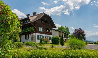 A charming Alpine house with a well-kept garden. Bright blue sky and a few trees in the background complement the idyllic scene.