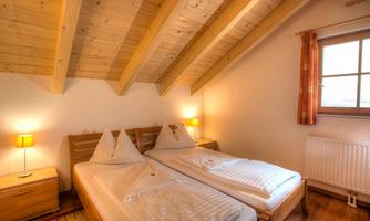 A cozy bedroom with two beds and wooden ceilings. Soft lighting from bedside lamps creates a pleasant atmosphere.