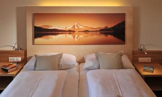 A cozy bedroom with two single beds and soft lighting.  
On the wall hangs a picture of a picturesque mountain landscape at sunset.