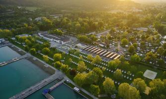 A stunning view of a campsite by the water, surrounded by lush greenery. The sunset bathes the landscape in warm light.