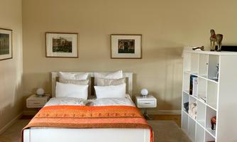 A modern bedroom with a white bed and an orange duvet. There are two nightstands and a bookshelf on the wall.