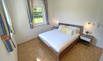 A bright bedroom with a large bed and colorful curtains. The room is simply and modernly furnished, ideal for a relaxing getaway.