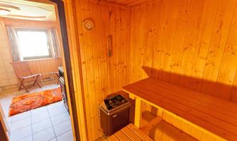 A cozy sauna with wooden paneling and a bench for sitting. In the background, a window and a side chair are visible.