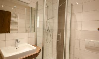 A modern bathroom with a glass shower, a sink on wood, and a toilet. The walls are brightly tiled, and the lighting is pleasant.