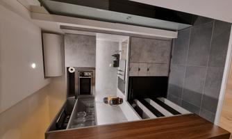 A modern kitchen with gray walls and wooden shelves. It features a stove, a sink, and storage space.