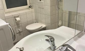A modern bathroom with a smooth white surface and a large mirror. Two black cups are placed on the sink, and fresh towels are neatly folded.