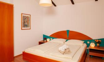 A cozy bedroom with a large bed and colorful walls. Flowers are placed on the nightstand, and a wall decoration is visible.