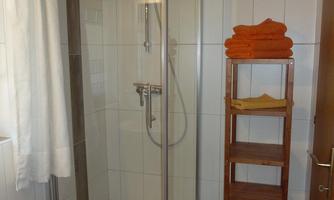 A modern bathroom with a shower and bright tiles. A wooden towel rack stands next to the shower.