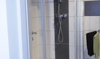 A modern shower with glass partition and timeless tile design. Towels hang on the wall, and the space is bright and inviting.