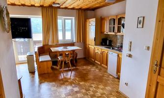 A cozy kitchen with wooden shelves and a dining table. Large windows provide plenty of light and a view outside.