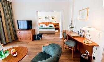 A modern hotel room with a cozy bed, television, and desk. The room is bright and inviting, with a table and a fruit basket.