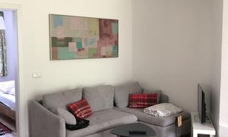 A cozy living room with a gray sofa and a small table. A modern piece of art hangs on the wall and there is a dining table in the foreground.