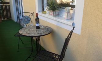 A small balcony with a round table and two chairs. On the table, there is a bottle of wine and a glass.