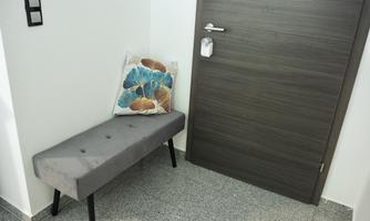 A simple bench with a padded surface is against a wall. Next to the bench is a pillow with a colorful floral pattern.