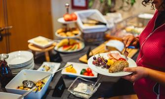 A buffet with a selection of fresh fruits, pastries, and other treats. A person is currently choosing their food on a plate.