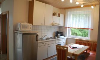 A modern kitchen with bright walls and wooden details. A table with chairs is at the center, complemented by appliances like a refrigerator and a microwave.
