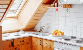 A cozy kitchen in the attic with wooden cabinets and a window. On the countertop, there are some cups and fresh fruit.