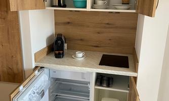 A modern kitchen with wooden shelves and an integrated refrigerator. On the countertop, a coffee machine and a cup are visible.