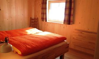A cozy bedroom with wooden interior. There is a large bed with orange blankets and a windowsill with curtains.