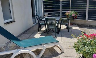 A cozy terrace with a deck chair, a table, and chairs.  
Surrounded by flowers and a sunshade, overlooking a beautiful landscape.