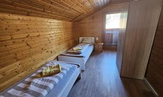 A cozy room with wooden paneling and two single beds. The window offers a view outside and the room feels bright and inviting.
