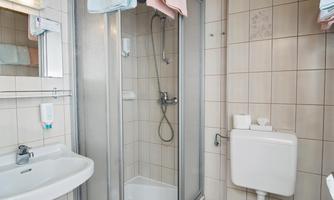 A small bathroom with a shower, a sink, and a toilet. The walls are tiled and there is a wooden ceiling.