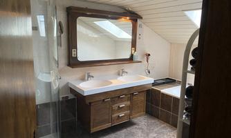 A modern bathroom with two sinks and a large mirror. It has bright walls and skylight lighting.