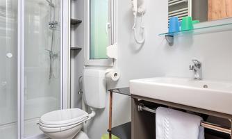 A modern bathroom with a shower, toilet, and sink. The furnishings are simple and functional, with fresh towels and a textured floor.
