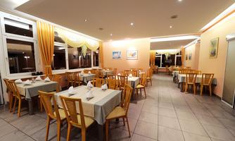 A cozy restaurant with wooden furniture and round tables. The walls are painted in soft shades of orange, and there are large windows with curtains.