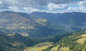A breathtaking mountain landscape with gentle hills and a clear sky. Green meadows and forests characterize the view.
