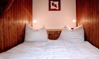 A cozy bedroom with two single beds and wooden walls. A small picture hangs on the wall, and two bedside lamps provide soft light.