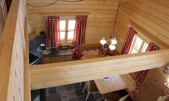 A cozy wooden apartment with a large dining table and a modern kitchen. The windows are decorated with red curtains and there is a warm, inviting atmosphere.
