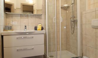 A modern bathroom with a shower cubicle and a sink. The walls are tiled, and there is a large mirror above the sink.
