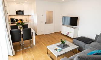 A modern apartment with an open kitchen and a dining area. The living space is bright and inviting, with cozy furnishings.