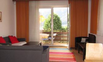 A bright living room with a sofa and a table. The doors lead to a balcony with a view of the greenery.