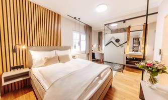 A modern bedroom with a large bed and wood paneling on the wall. There is also a small table and fresh flowers on a nightstand.