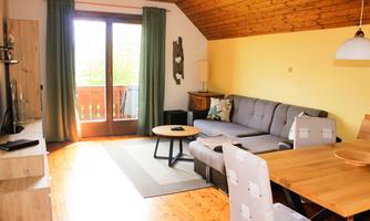 A bright living room with a gray sofa and wooden flooring. Large windows with balcony doors let in plenty of light.