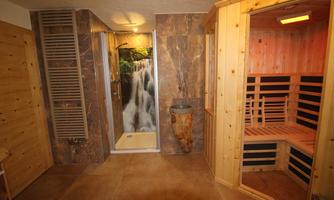 A modern spa with a wooden sauna and a shower that features a waterfall illusion. The walls are adorned with stone tiles, creating a soothing atmosphere.