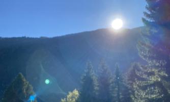 A clear sky above a wooded mountain. The sun shines brightly and illuminates the landscape.