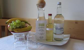 A tray with two glass containers, a carafe, and various drinks. In the background, there is a bowl of bananas and grapes.