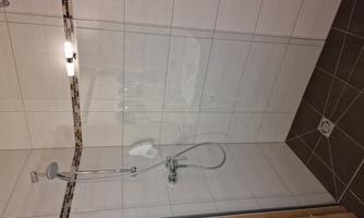 A modern shower with smooth tiles and a glass wall. The features include a rain shower and a hand-held showerhead.