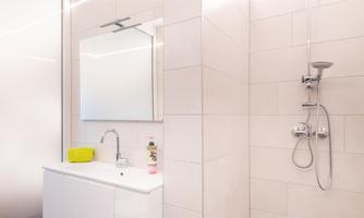 A modern bathroom with a shower and a white sink. A large mirror is mounted on the wall.