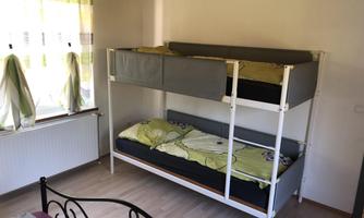 A simple room with a bunk bed and a window with green curtains. The floor is made of light wood and the walls are painted in a light color.