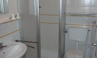 A small bathroom with a shower, a sink, and a toilet. The walls are tiled and kept in a bright white.