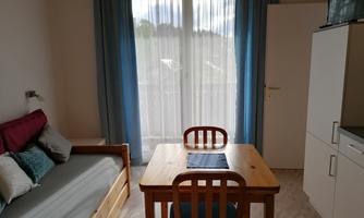 A bright room with a sofa, a table, and chairs. Large windows let in a lot of light.