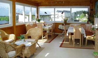 A cozy conservatory with rattan furniture and tables. Generous windows offer a view of the surroundings and let in plenty of light.