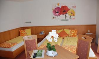 A cozy guest room with two single beds and a table. A colorful painting of flowers hangs on the wall.