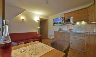 A cozy living and dining room with wooden details. A fully equipped kitchen and a red sofa create an inviting atmosphere.