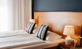 A cozy bedroom with a double bed and modern cushions. Next to the bed are nightstands with lamps and soft curtains.