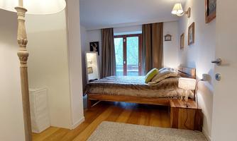 A cozy bedroom with a large bed, a carpet, and a window with curtains. In the corner stands a floor lamp.
